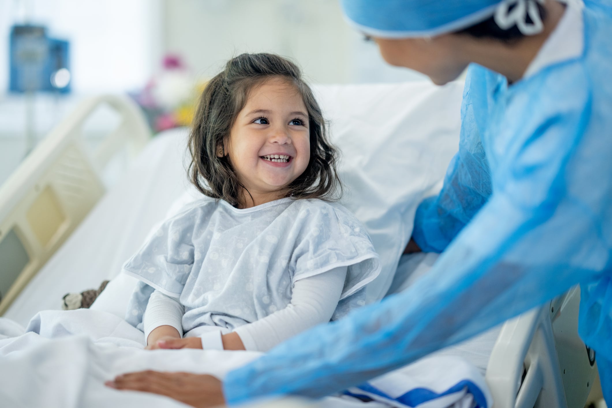 A female doctor of Indian decent checks in on a young female patient after her surgery. The patient is sitting up in bed and appears happy.