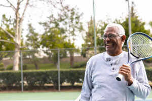 Senior man smiling holding a tennis racket on the tennis court