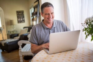 A middle-aged man typing on laptop at kitchen table