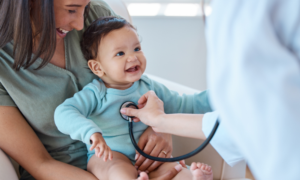 A provider probing a baby with a stethoscope with the mother holding the baby smiling